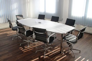 Immagine che rappresenta un ufficio con tavolo da lavoro attorniato da 8 sedie vuote